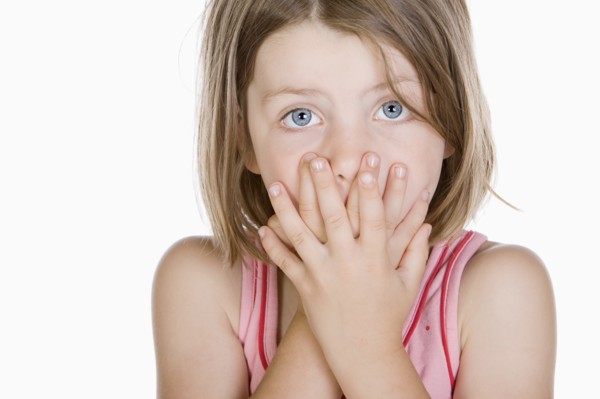 Studio portrait of girl (6-7) covering mouth. Photo : Justin Paget