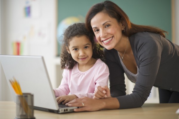 Girl (6-7) with female teacher using laptop in classroom.