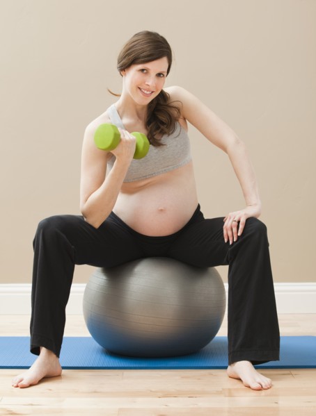 Young pregnant woman exercising with dumbbells and fitness ball. Photo : Mike Kemp