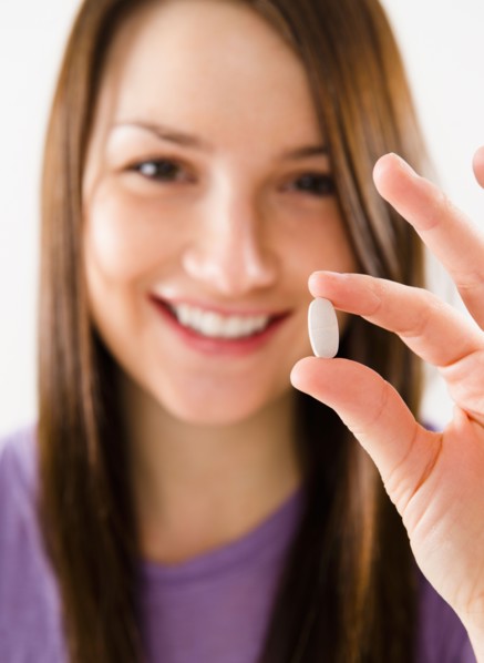 Portrait of smiling young woman holding pill. Photo : Jamie Grill Photography
