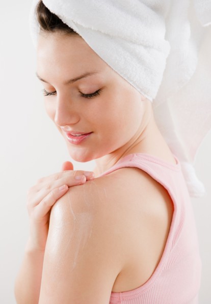 Young woman applying moisturizer on shoulder. Photo : Jamie Grill Photography