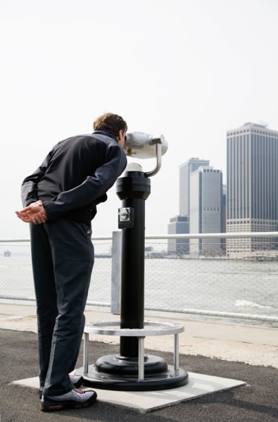 USA, New York City, Manhattan, man looking at skyline through telescope. Photo : Maisie Paterson