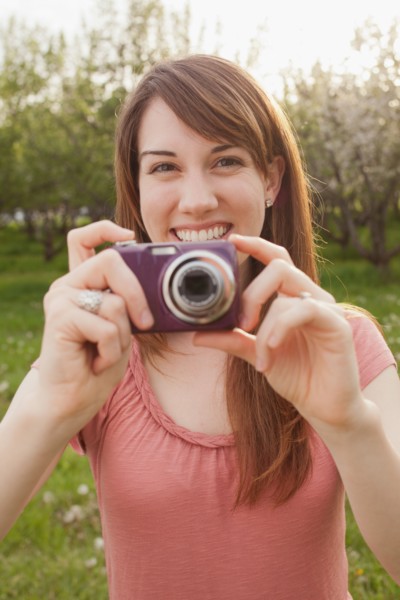 USA, Utah, Provo, Young woman holding digital camera in orchard. Photo : Mike Kemp