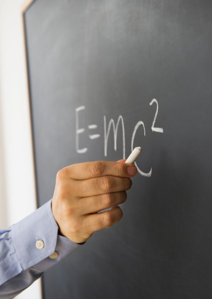 Close-up of man's hand writing theory of relativity formula on blackboard.