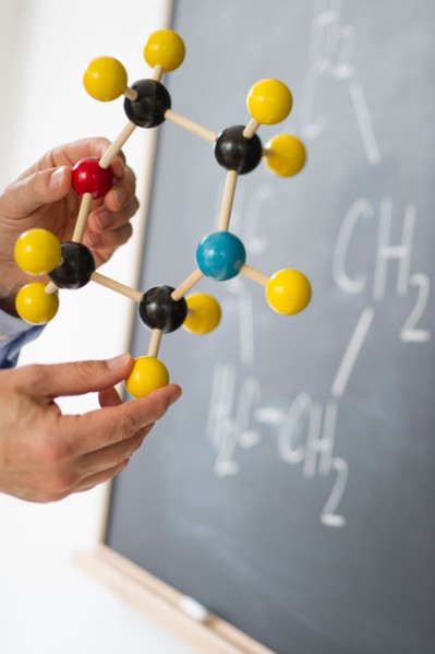 Close-up of man's hands holding molecule model, blackboard in background.