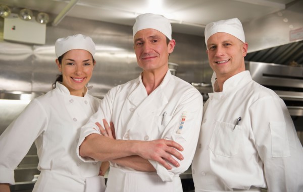 Three chefs posing in kitchen.