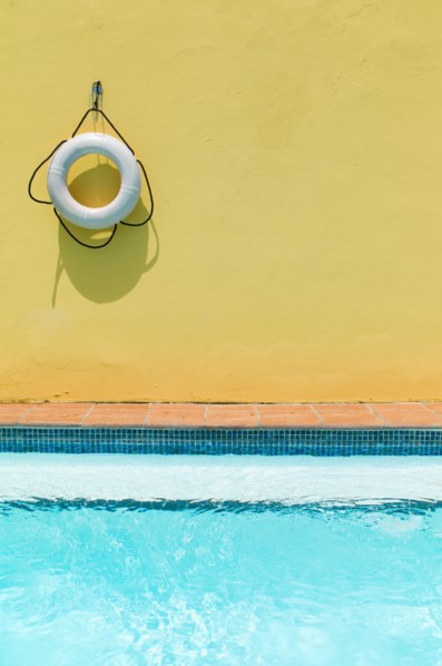 Lifebelt hanging on yellow wall by swimming pool.