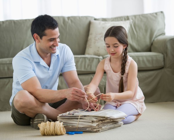 Father and daughter (8-9) wrapping up wastepaper bundle.