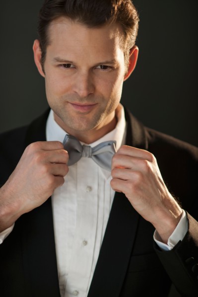 Studio portrait of bridegroom adjusting bow tie.