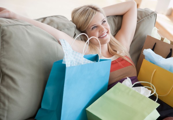 Young woman sitting on sofa surrounded by shopping bags. Photo: Jamie Grill