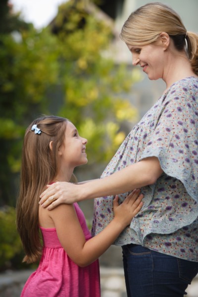 Pregnant mother standing face to face with daughter (6-7) . Photo : Rob Lewine