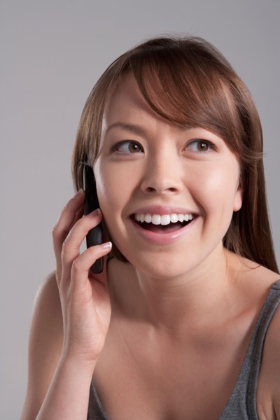 Portrait of young smiling woman using mobile phone, studio shot. Photo : Rob Lewine