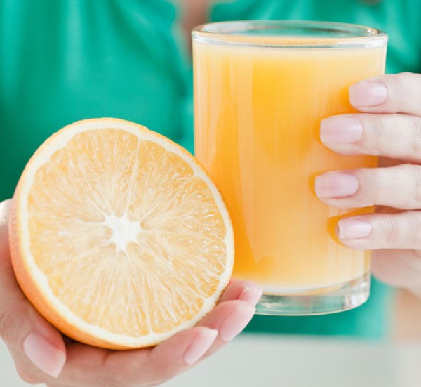 Close up of woman's hands holding half of orange and glass of juice. Photo : Jamie Grill