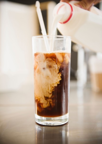 Close up of hand pouring milk into iced coffee. Photo : Jamie Grill
