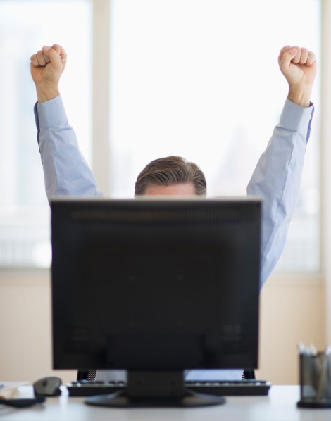 Businessman raising hands from behind computer.