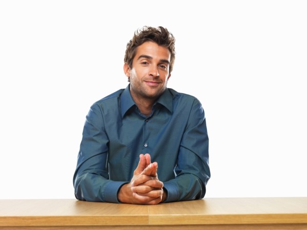 Smiling business man sitting at table with hands clasped. Photo : momentimages