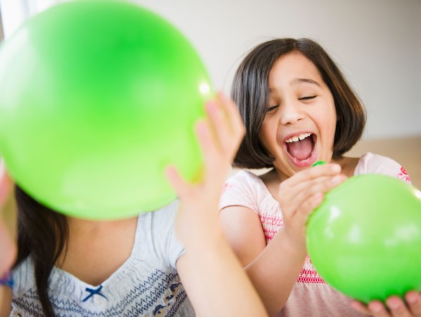 Close up of two girl's (8-9, 10-11) playing with green balloons. Photo : Jamie Grill