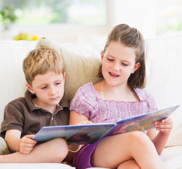 Close up of girl (6-7) and boy (4-5) reading book on sofa. Photo : Daniel Grill