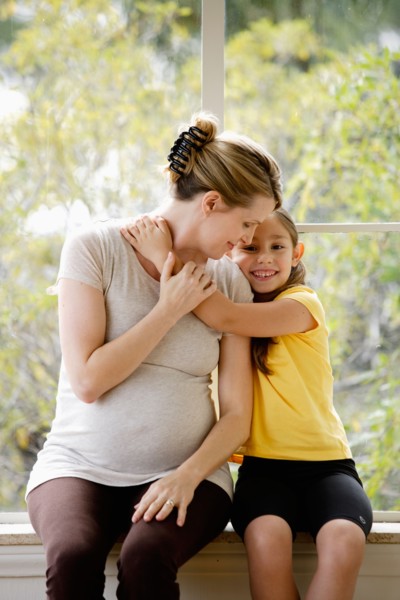 Daughter (6-7) sitting next to pregnant mother, embracing. Photo: Rob Lewine