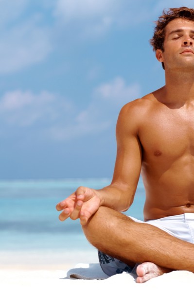 Cropped image of a young man meditating at the beach in a lotus position. Photo : momentimages