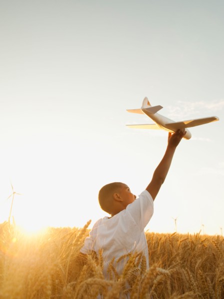 Boy (10-11) playing with toy aeroplane in wheat field.