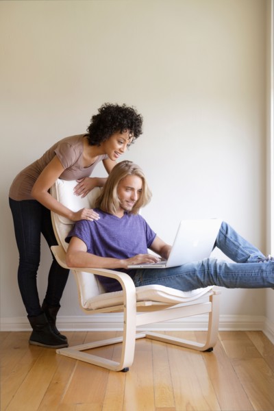 Young woman looking at man using laptop at home. Photo : Rob Lewine
