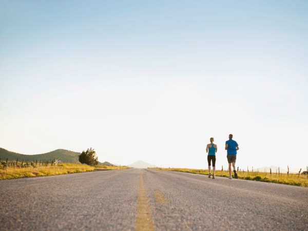 Mid adult couple running on empty road. Photo: Erik Isakson