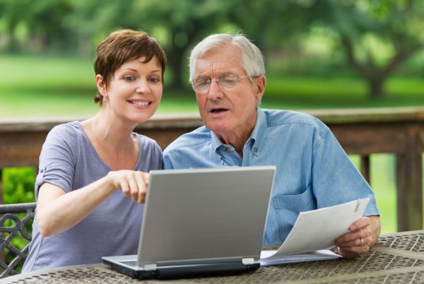 Senior father and adult daughter using laptop on porch.