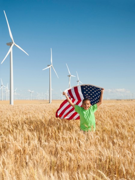USA, Oregon, Wasco, Boy (8-9) flying american flag in wheat field with wind turbines in background.