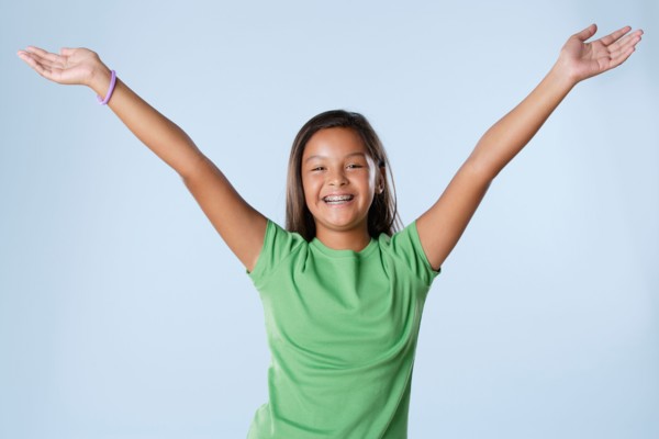 Studio portrait of girl smiling (10-11) with raised hands. Photo : Rob Lewine