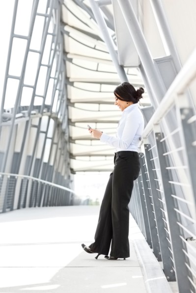 Young businesswoman on walkway, using cell phone. Photo: Take A Pix Media