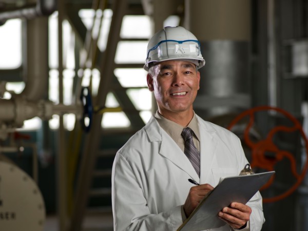 Man in lab coat and hard hat holding clipboard. Photo : db2stock