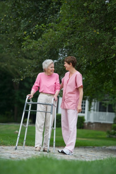 Senior woman walking with walker with help of nursing assistant.
