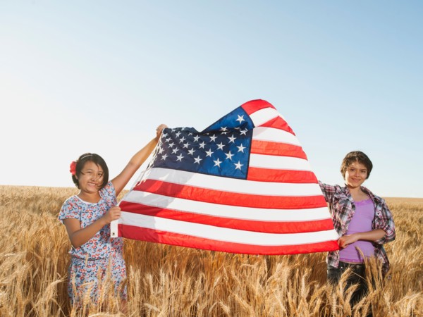 Girls (10-11, 12-13) holding american flag in wheat field.