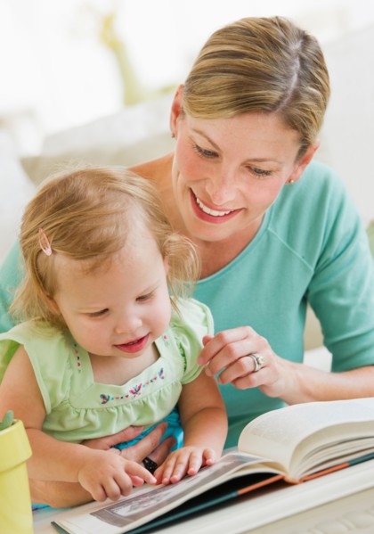 Mother with daughter (2-3) reading book in living room.