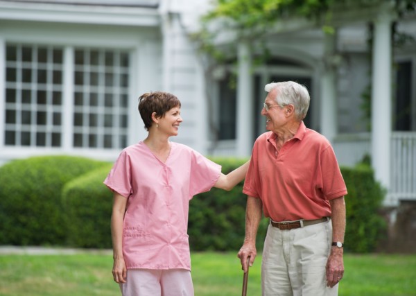 Senior man and nursing assistant walking in back yard.