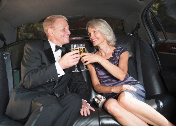 Parents of bride drinking champagne inside limousine.