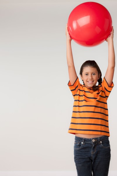Studio portrait of girl (8-9) holding red ball. Photo: Rob Lewine