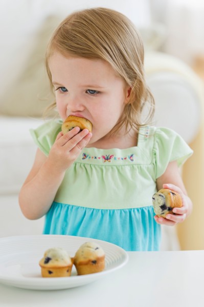 Girl (2-3) eating muffins.