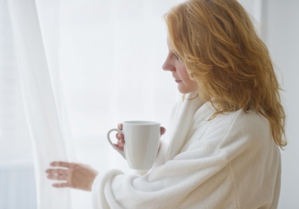 Woman in bathrobe looking out window.