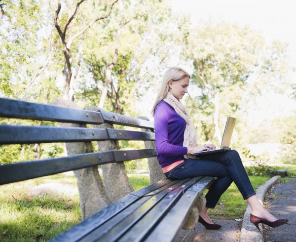 USA, New York, New York City, Manhattan, Central Park, Young woman sitting on bench and using