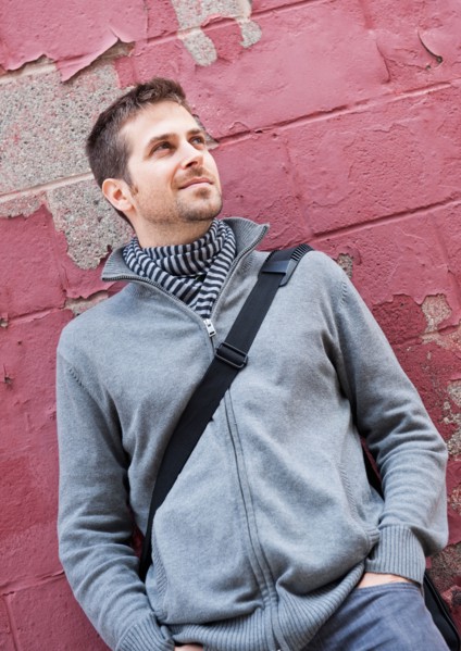 Man standing at front of old peeling red wall. Photo : Daniel Grill