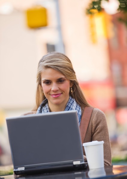 Young woman sitting with laptop in sidewalk cafe. Photo : Daniel Grill