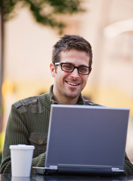Young woman sitting with laptop in sidewalk cafe. Photo : Daniel Grill