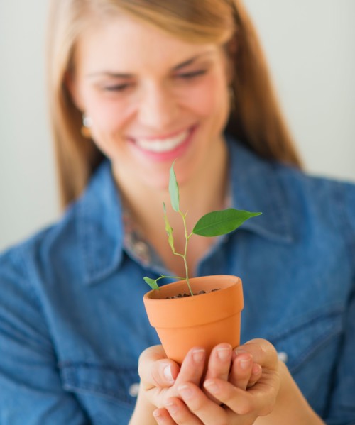 Young woman holding small plant. Photo : Daniel Grill