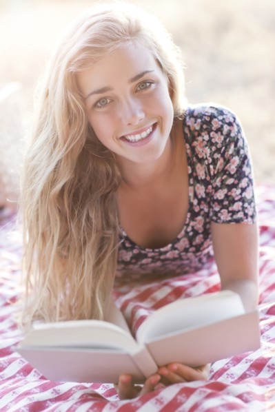 Happy teenage girl (16-17) reading book outdoors. Photo: Take A Pix Media