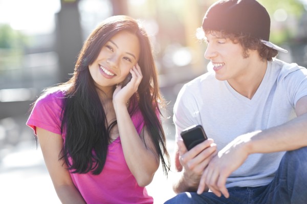 Young multi-racial couple sitting together playing with their mobile phones. Photo : Take A Pix