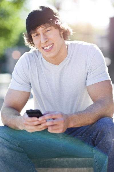 Young man sitting outdoors, text messaging. Photo : Take A Pix Media