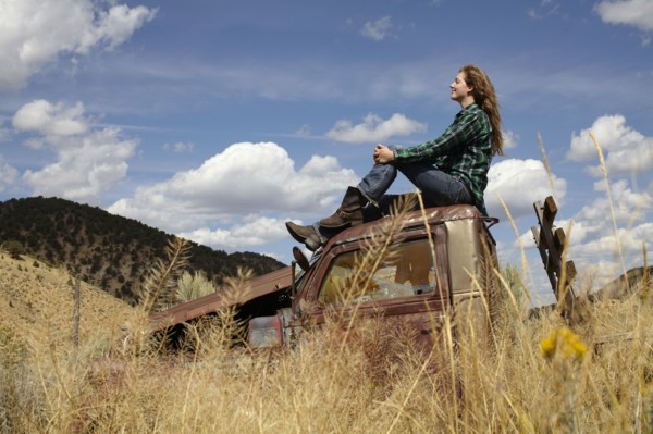 USA, Colorado, Woman resting on roof of abandoned truck in desert. Photo: John Kelly