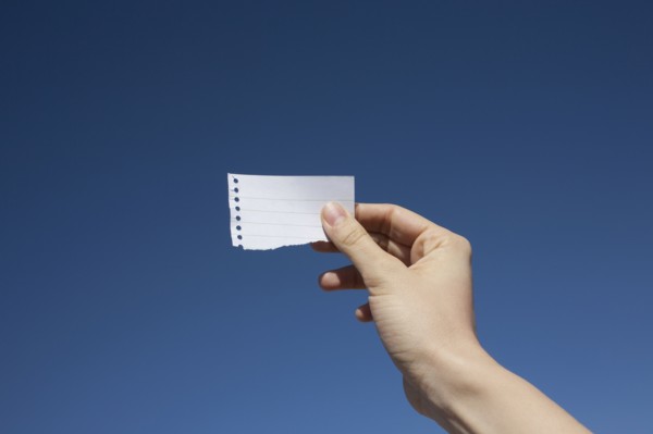 Hand of woman holding paper note against blue sky. Photo: Winslow Productions